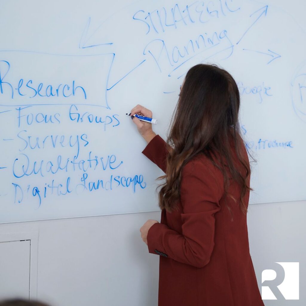 A woman writes research on a whiteboard about marketing during an economic downturn